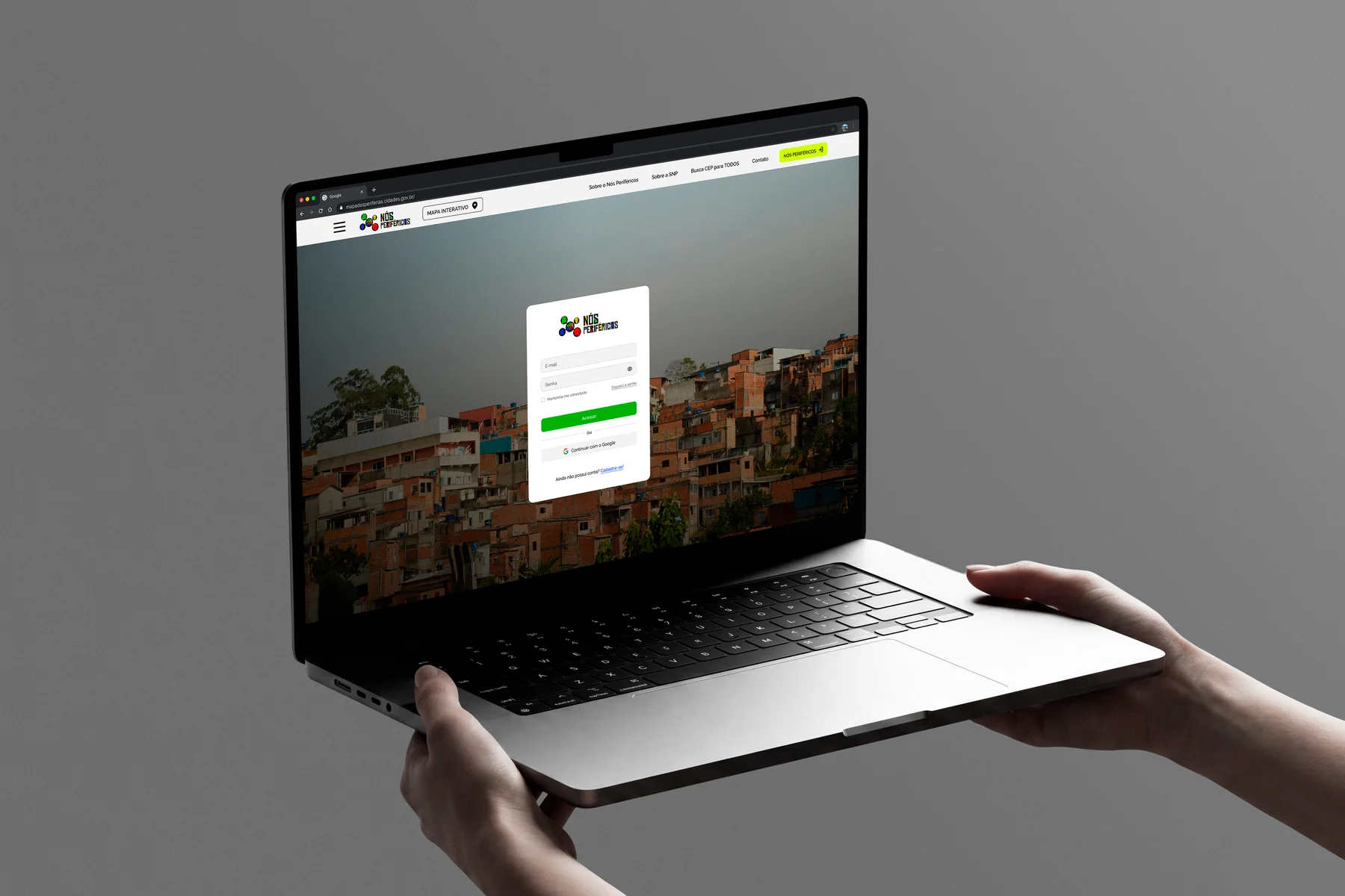 Notebook com a tela de entrada do Nós Periféricos: cartão de login com e-mail, senha, opção de entrar com o Google e link para cadastro, sobre a foto de uma comunidade