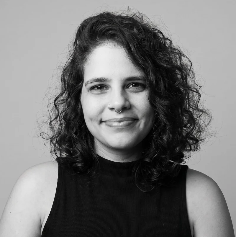 Retrato em preto e branco de Raiza Tomazoni, sorrindo, com cabelo cacheado